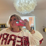 White crewneck sweatshirt with red plaid appliqué "MERRY" lettering, red ribbed collar trim, and balloon sleeves.