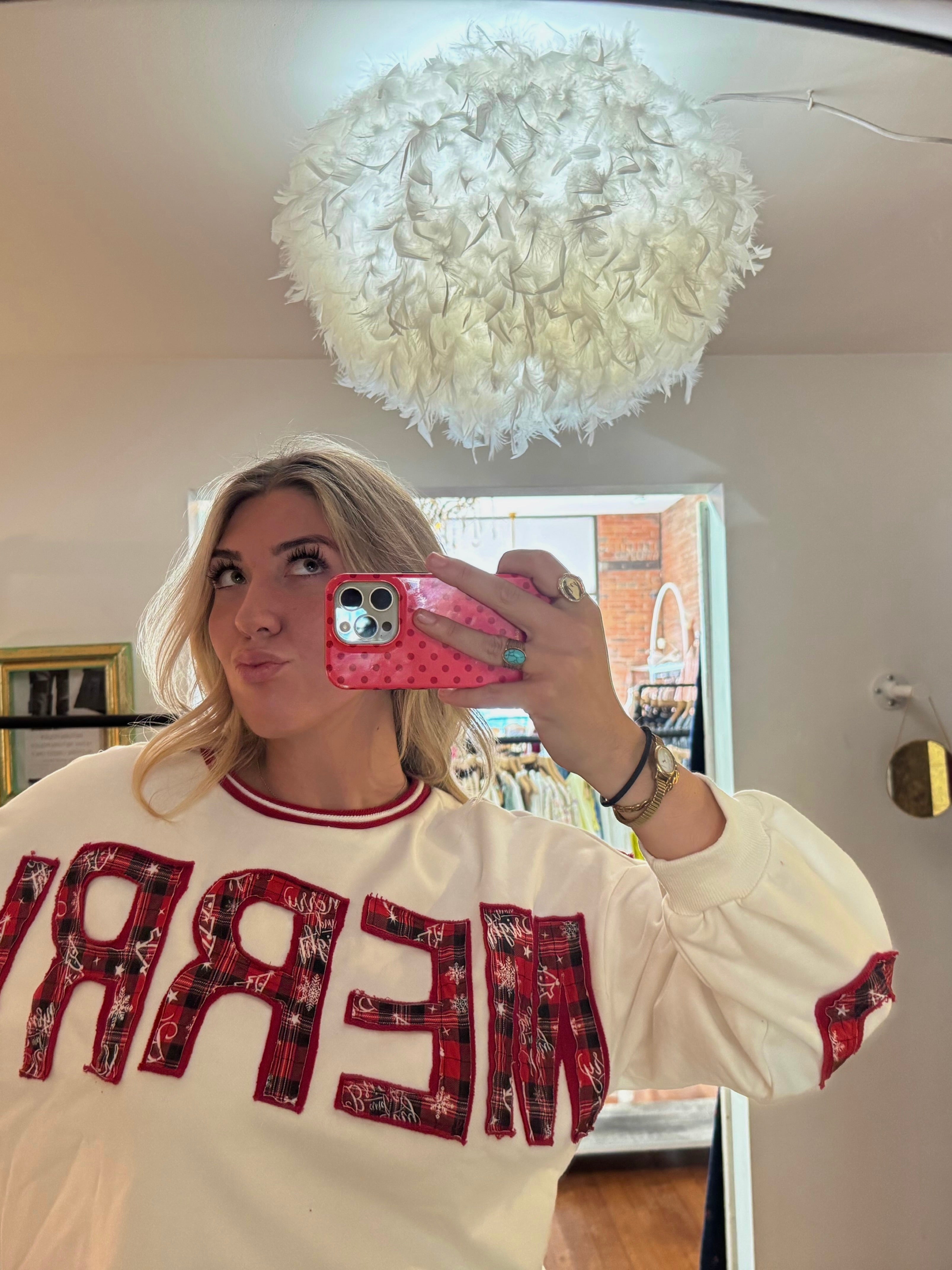 White crewneck sweatshirt with red plaid appliqué "MERRY" lettering, red ribbed collar trim, and balloon sleeves.