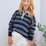 Navy blue striped knit polo sweater with gold and white stripes, gray collar, and button placket, styled with white trousers.