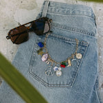 Gold chain necklace with colorful vintage-inspired charms laid on denim jacket with sunglasses