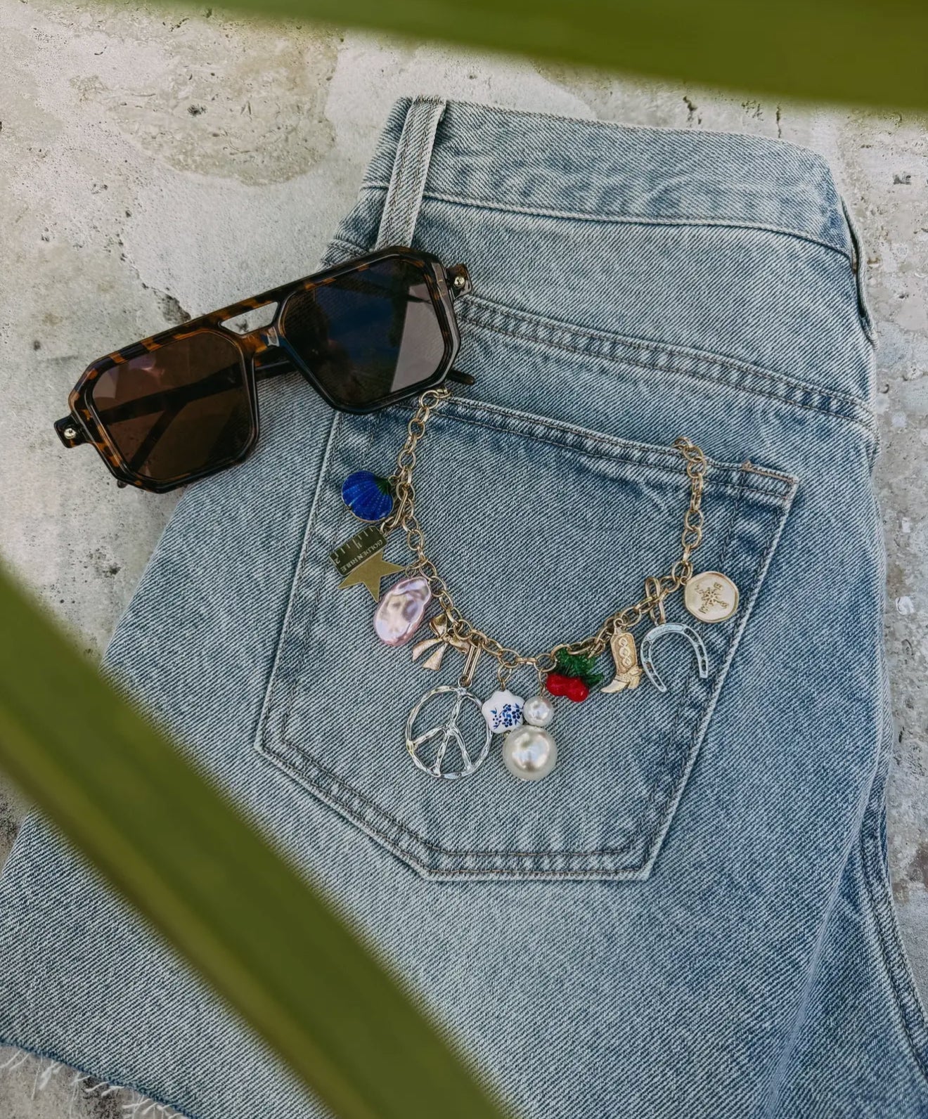 Gold chain necklace with colorful vintage-inspired charms laid on denim jacket with sunglasses