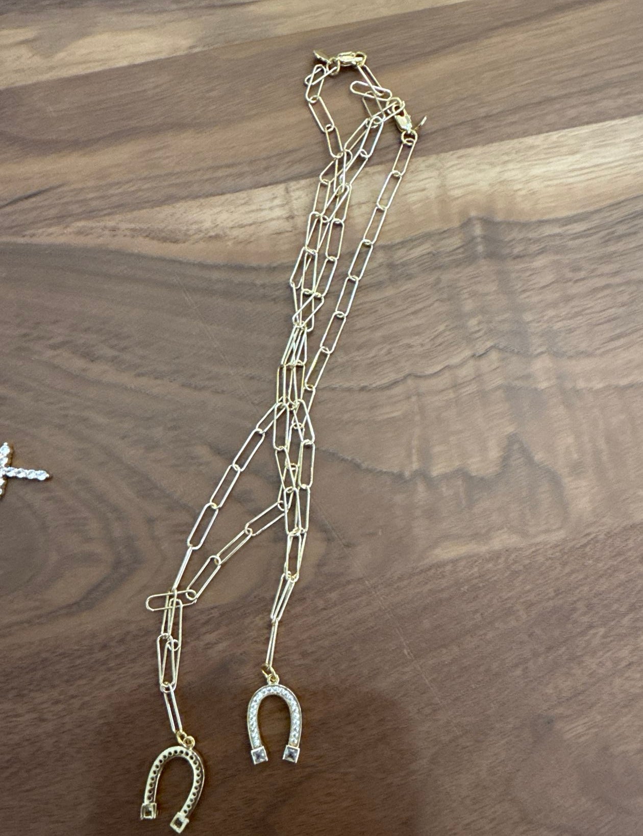 Gold tone layered chain necklace with horseshoe pendant charms on wood surface