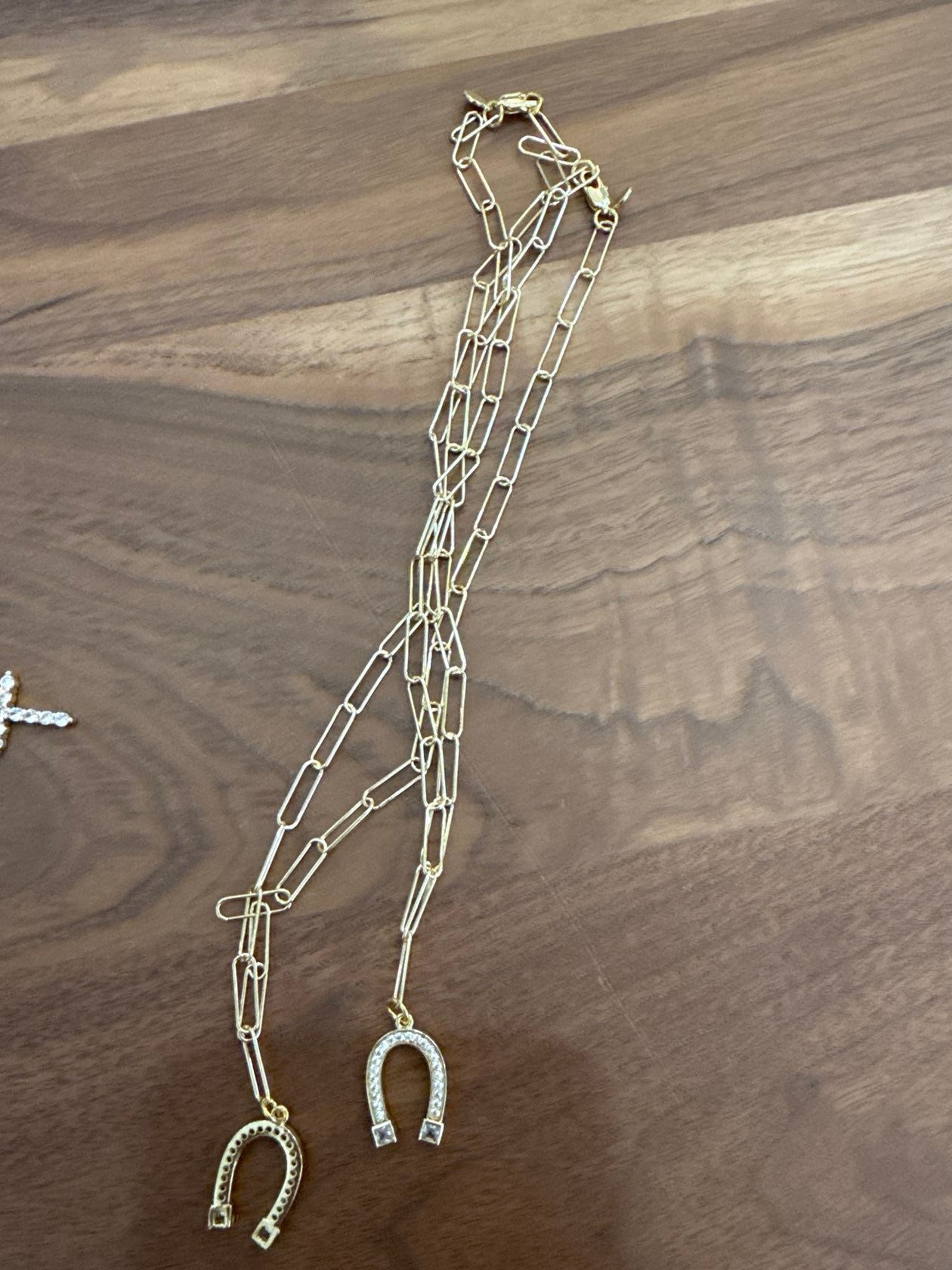 Gold tone layered chain necklace with horseshoe pendant charms on wood surface