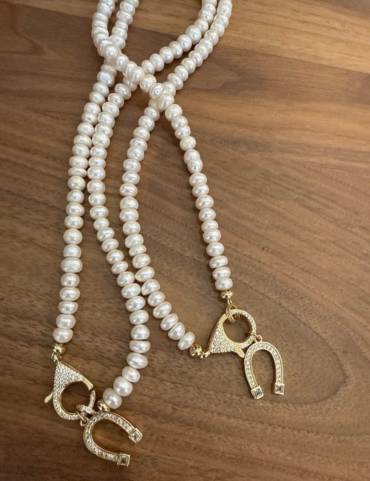 Two cream pearl necklaces with gold crystal toggle clasps on wood surface