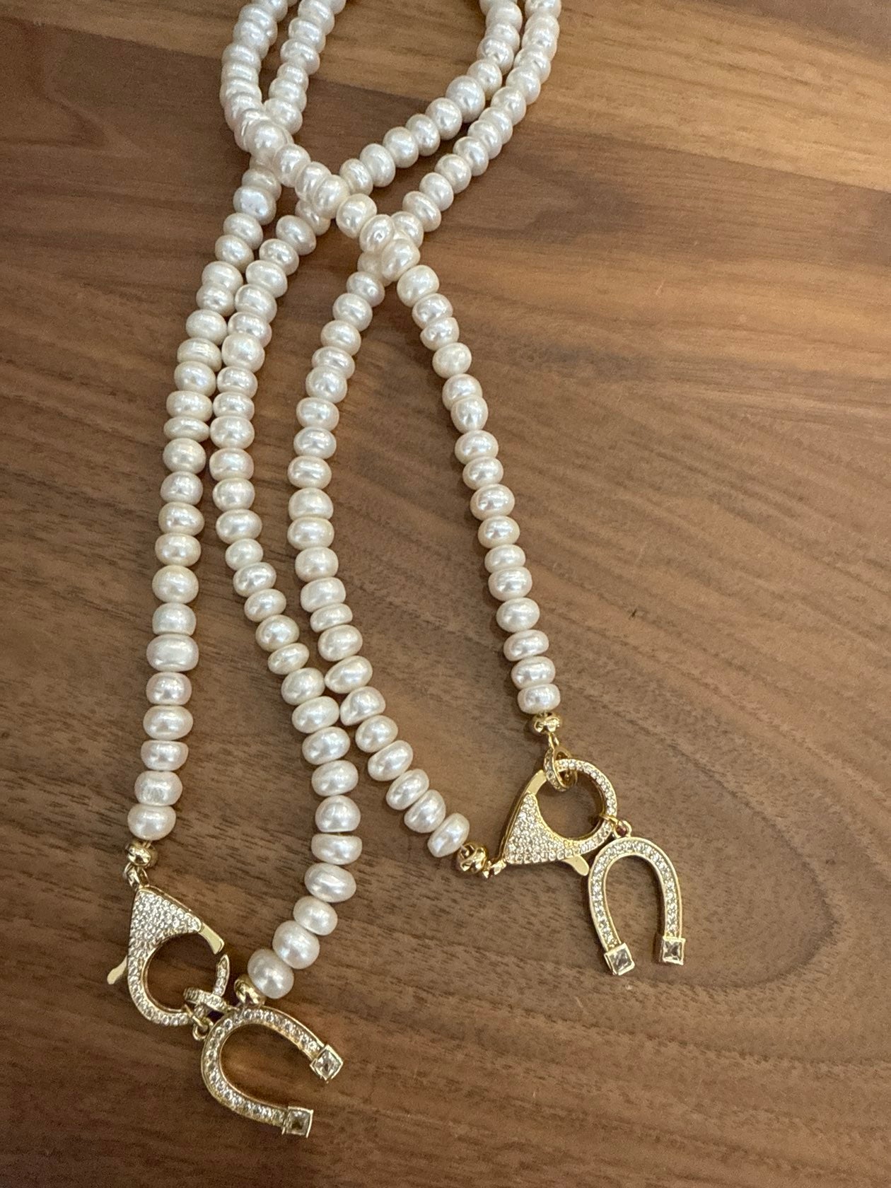 Two cream pearl necklaces with gold crystal toggle clasps on wood surface