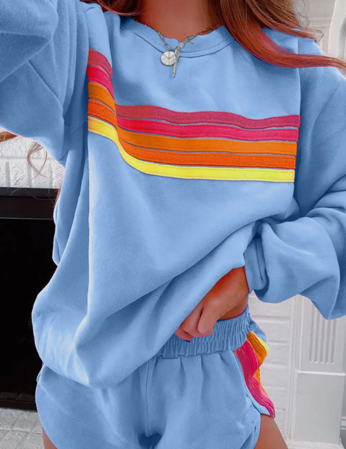 Woman wearing light blue loungewear shorts with rainbow striped side detail and matching hoodie