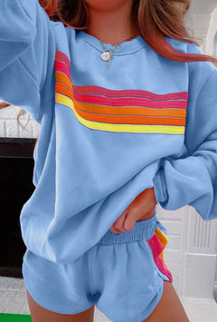 Woman wearing light blue loungewear shorts with rainbow striped side detail and matching hoodie