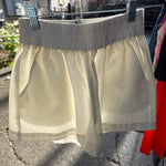 Cream off-white woven mini short with smocked elastic waistband displayed on outdoor clothing rack