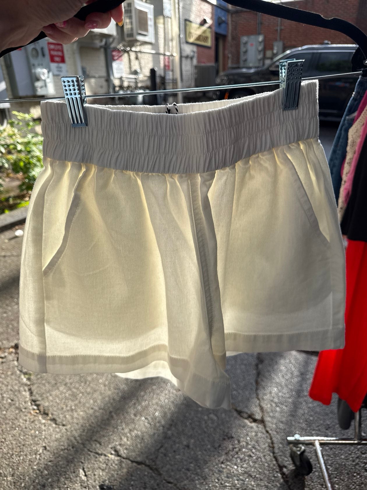 Cream off-white woven mini short with smocked elastic waistband displayed on outdoor clothing rack