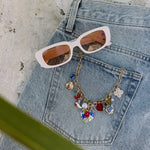 Light blue denim jeans with colorful charm necklace featuring floral and geometric pendants, styled with white sunglasses wit