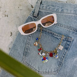 Light blue denim jeans with colorful charm necklace featuring floral and geometric pendants, styled with white sunglasses wit