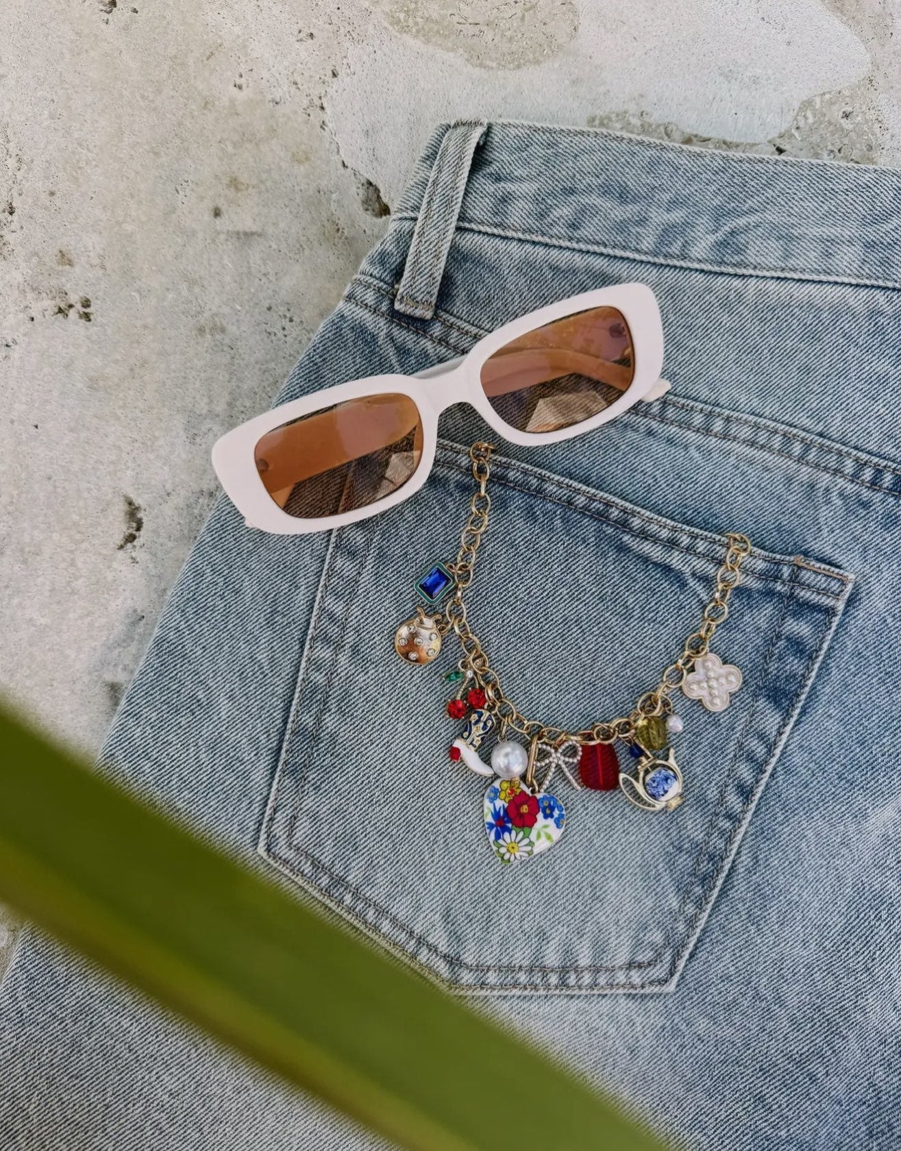 Light blue denim jeans with colorful charm necklace featuring floral and geometric pendants, styled with white sunglasses wit
