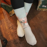 Cream colored crew socks with mountain landscape print featuring trees and pink sky details