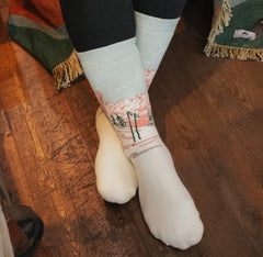Cream colored crew socks with mountain landscape print featuring trees and pink sky details