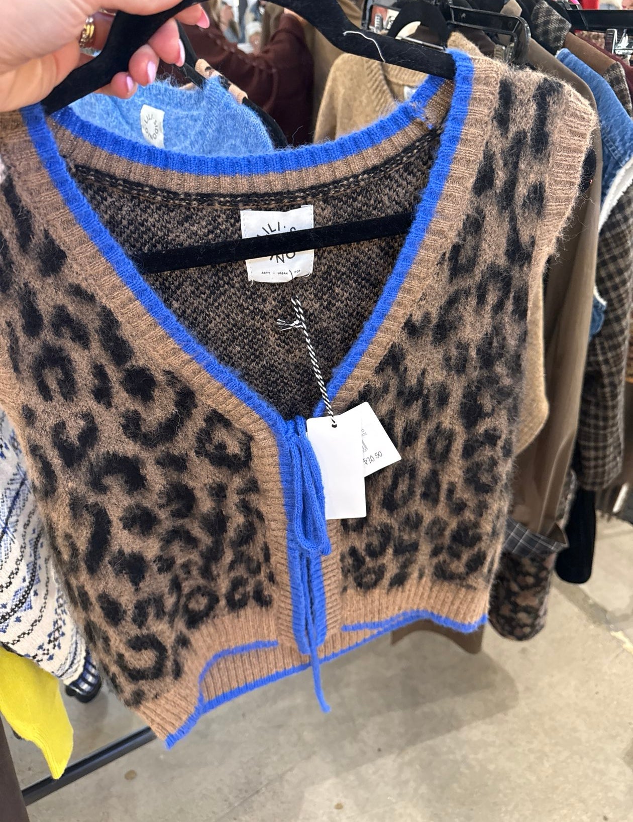 Cropped leopard print knit sweater vest with cobalt blue trim and tie neckline on hanger