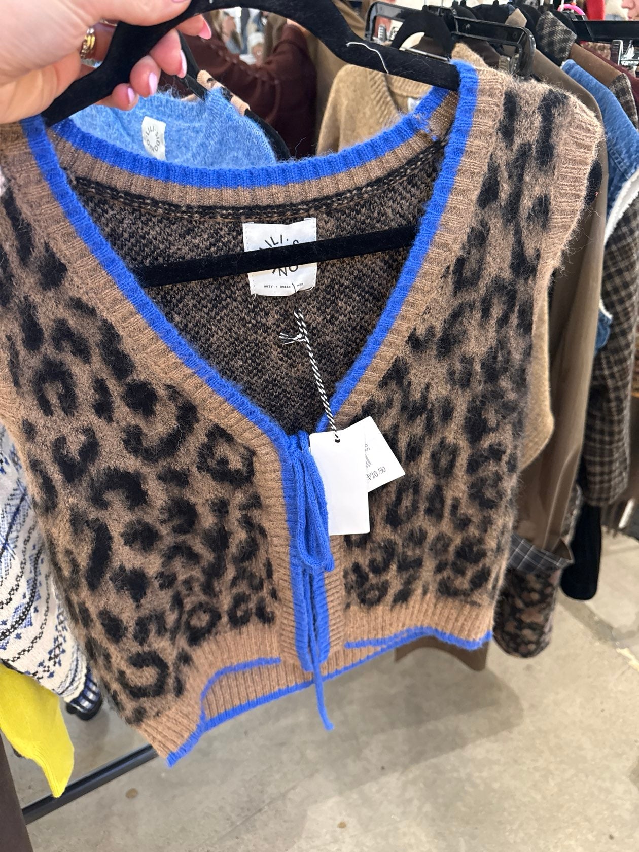 Cropped leopard print knit sweater vest with cobalt blue trim and tie neckline on hanger