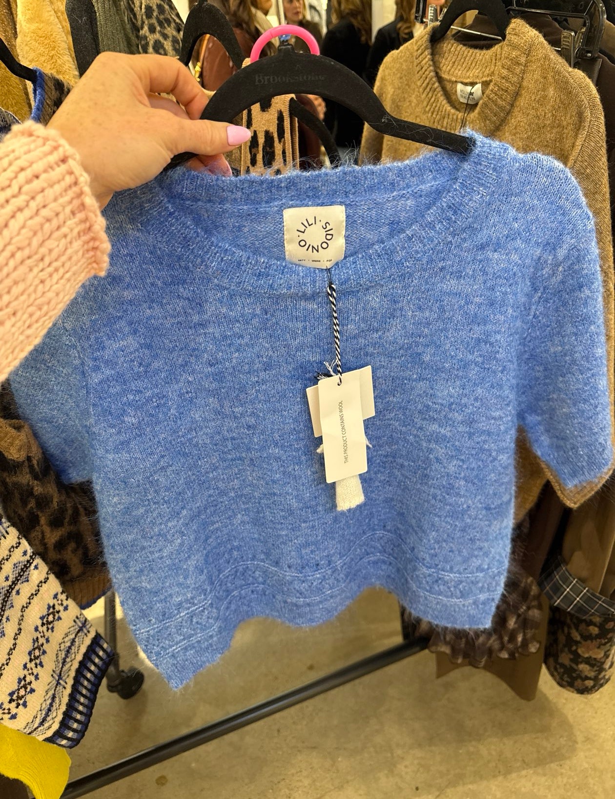 Cropped periwinkle blue wool knit top with scalloped hem and short sleeves on hanger