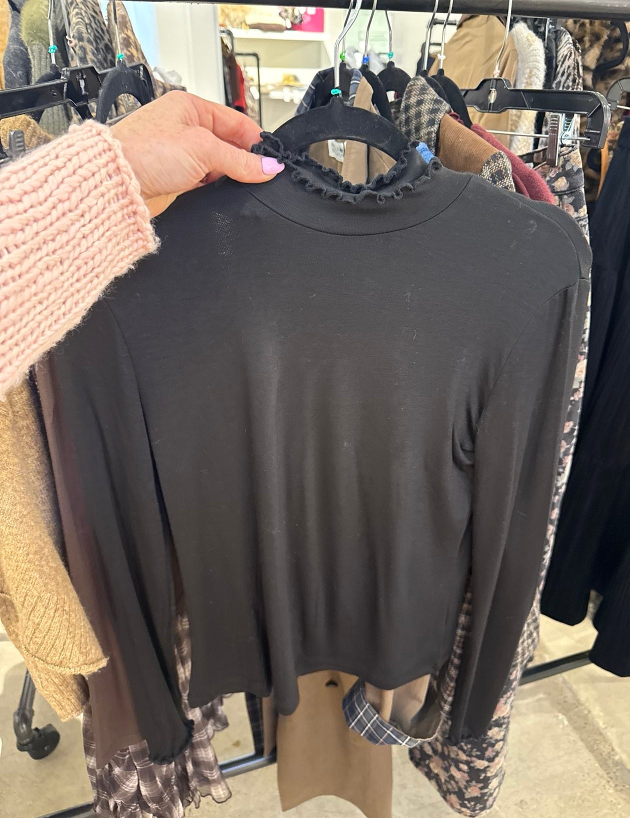 Black long sleeve mock turtleneck top with ruffle lettuce edge neckline on a hanger