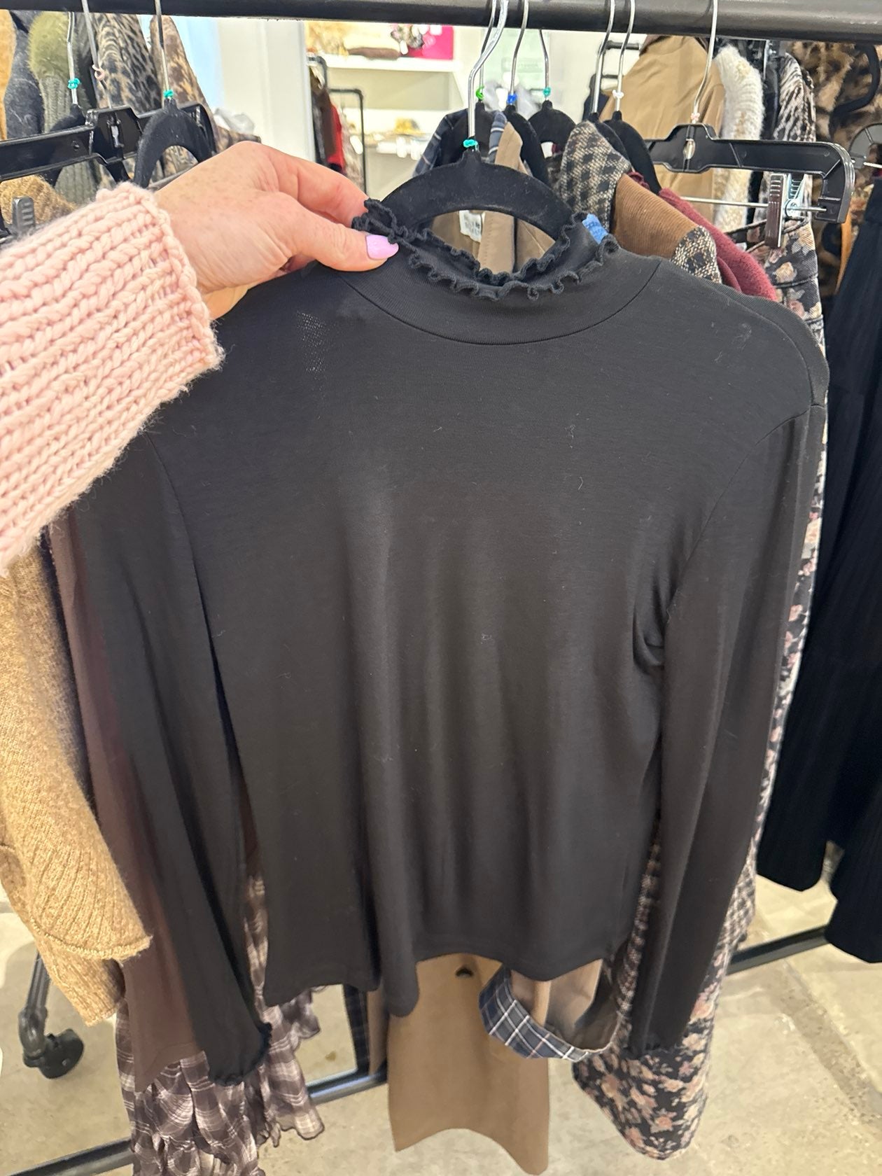 Black long sleeve mock turtleneck top with ruffle lettuce edge neckline on a hanger