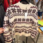 Cream Fair Isle knit sweater with burgundy and mauve snowflake pattern hanging on a boutique rack