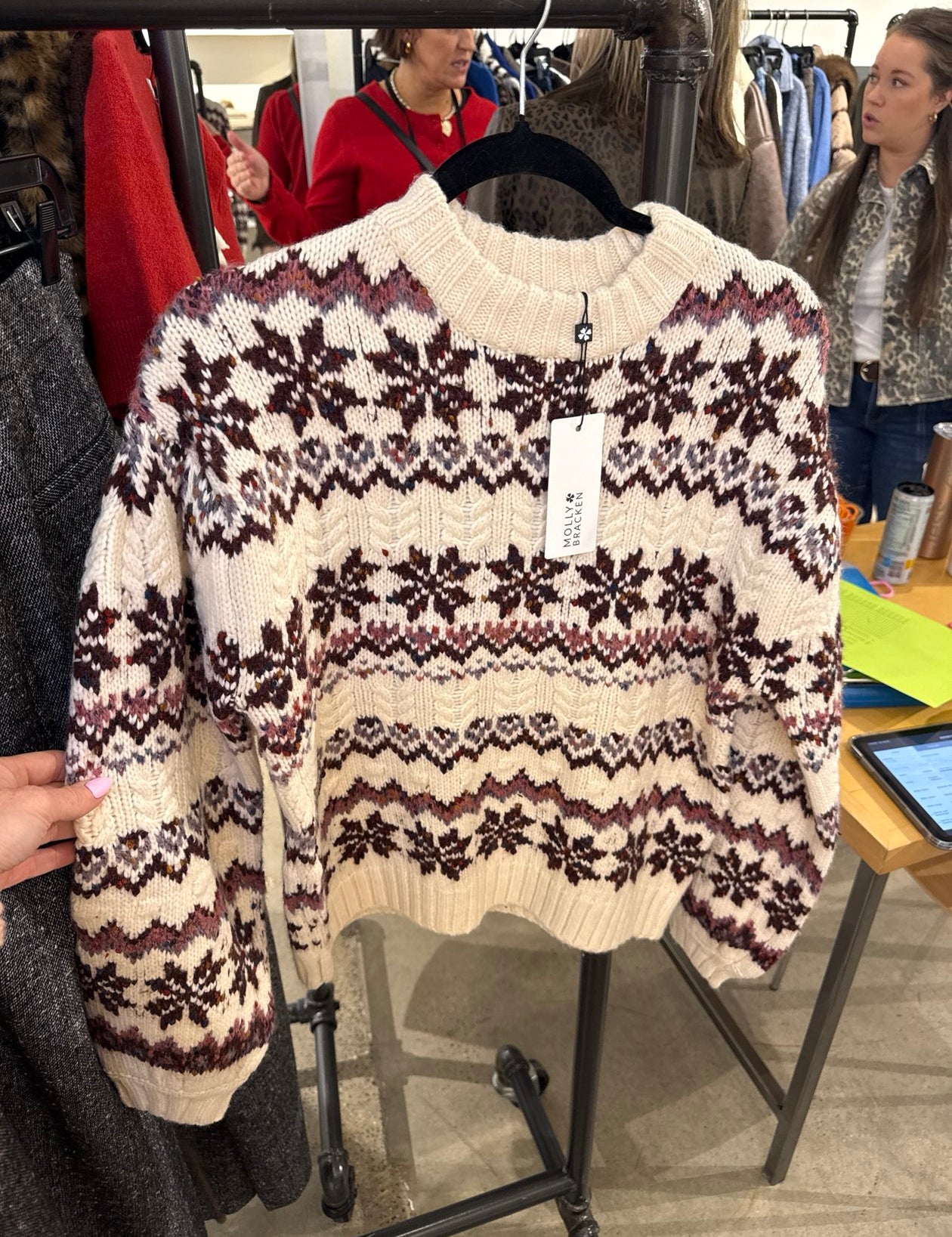 Cream Fair Isle knit sweater with burgundy and mauve snowflake pattern hanging on a boutique rack