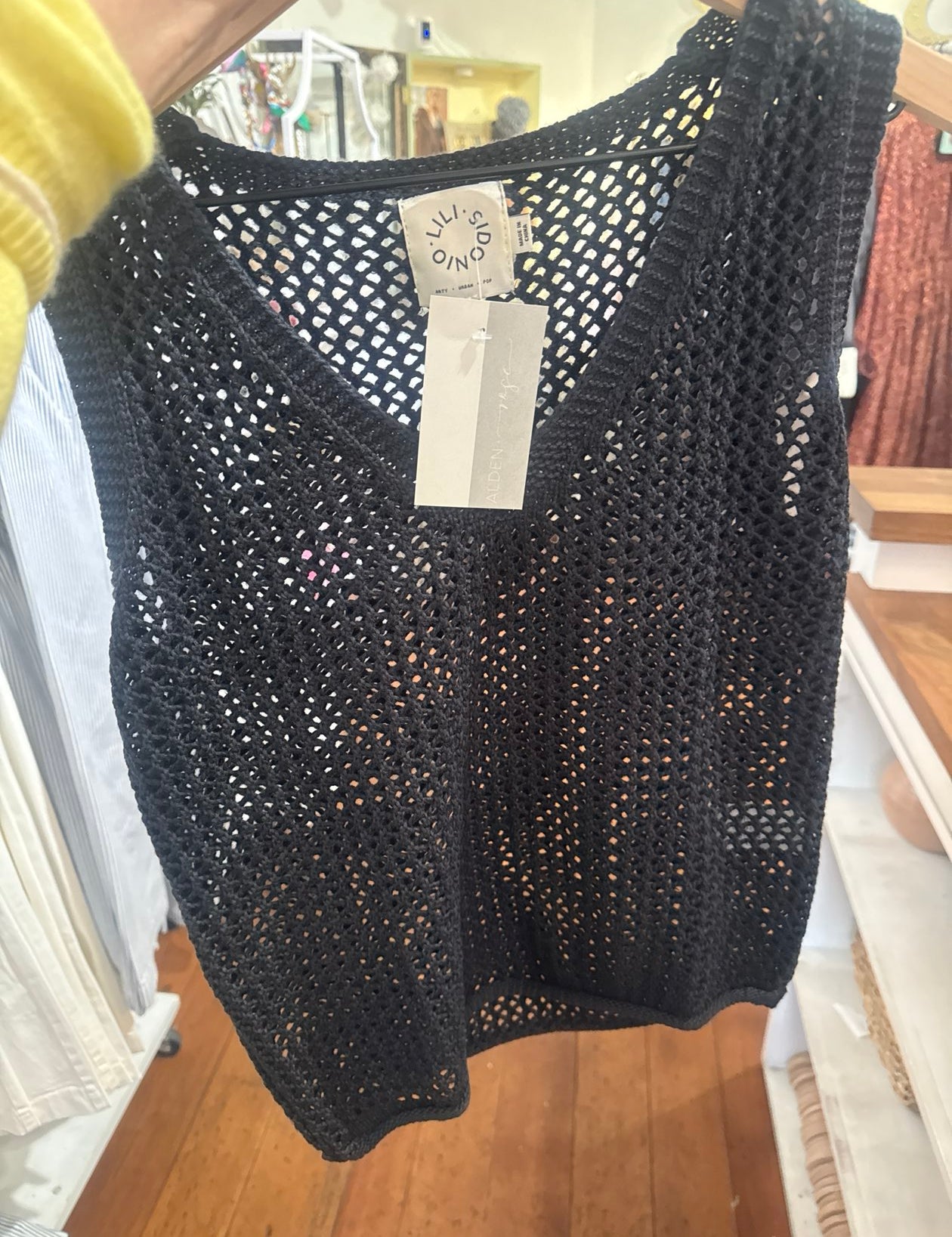 Black crochet knit sleeveless tank top with open weave pattern displayed on hanger