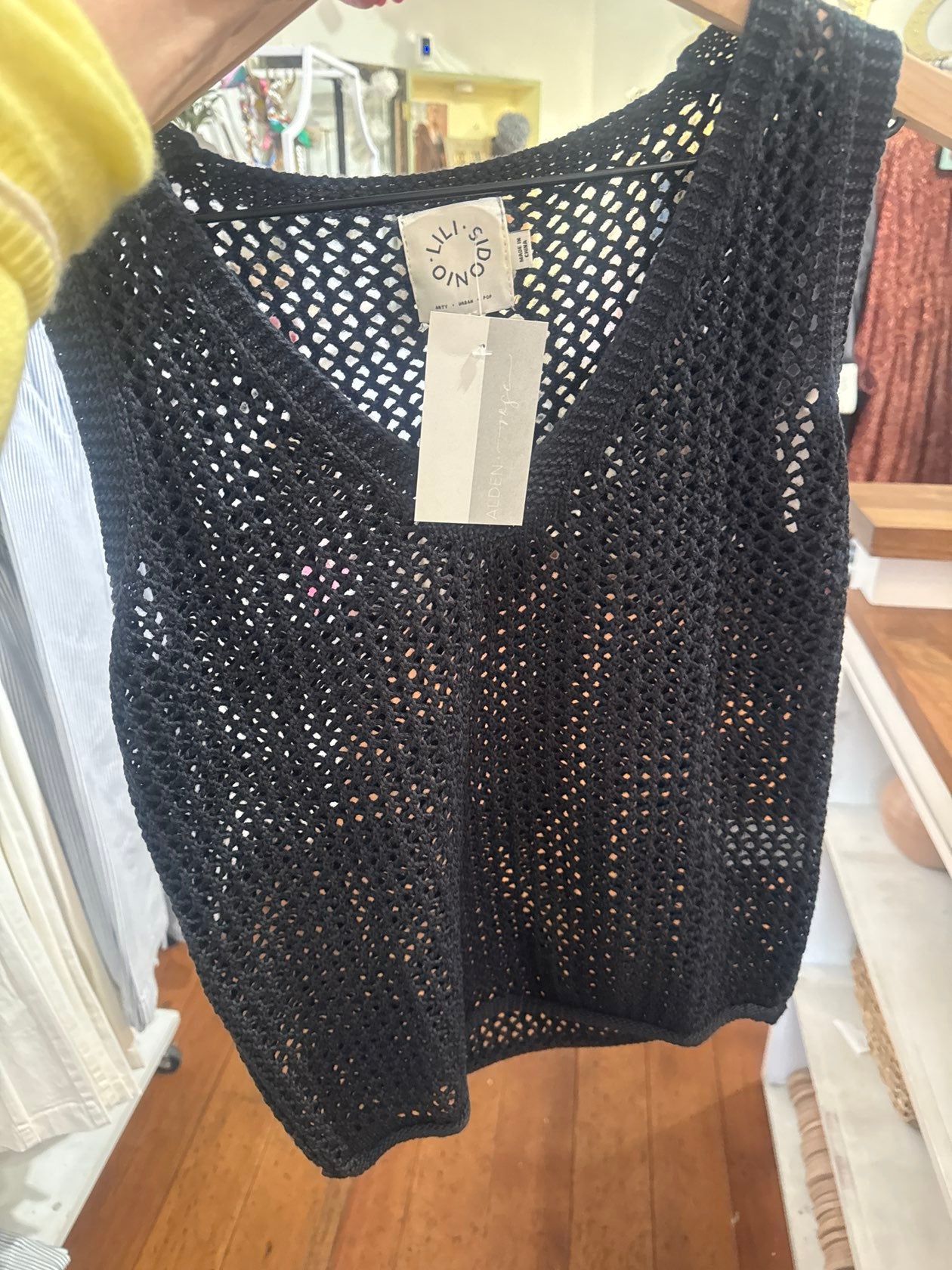 Black crochet knit sleeveless tank top with open weave pattern displayed on hanger
