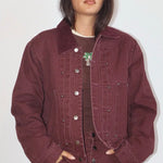 Oversized burgundy denim bomber jacket with silver snap buttons, corduroy collar, and palm tree brooch detail.