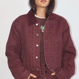 Oversized burgundy denim bomber jacket with silver snap buttons, corduroy collar, and palm tree brooch detail.