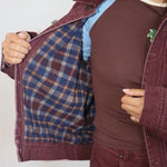 Burgundy flannel-lined denim bomber jacket shown open, revealing blue plaid interior lining, styled with matching trousers.