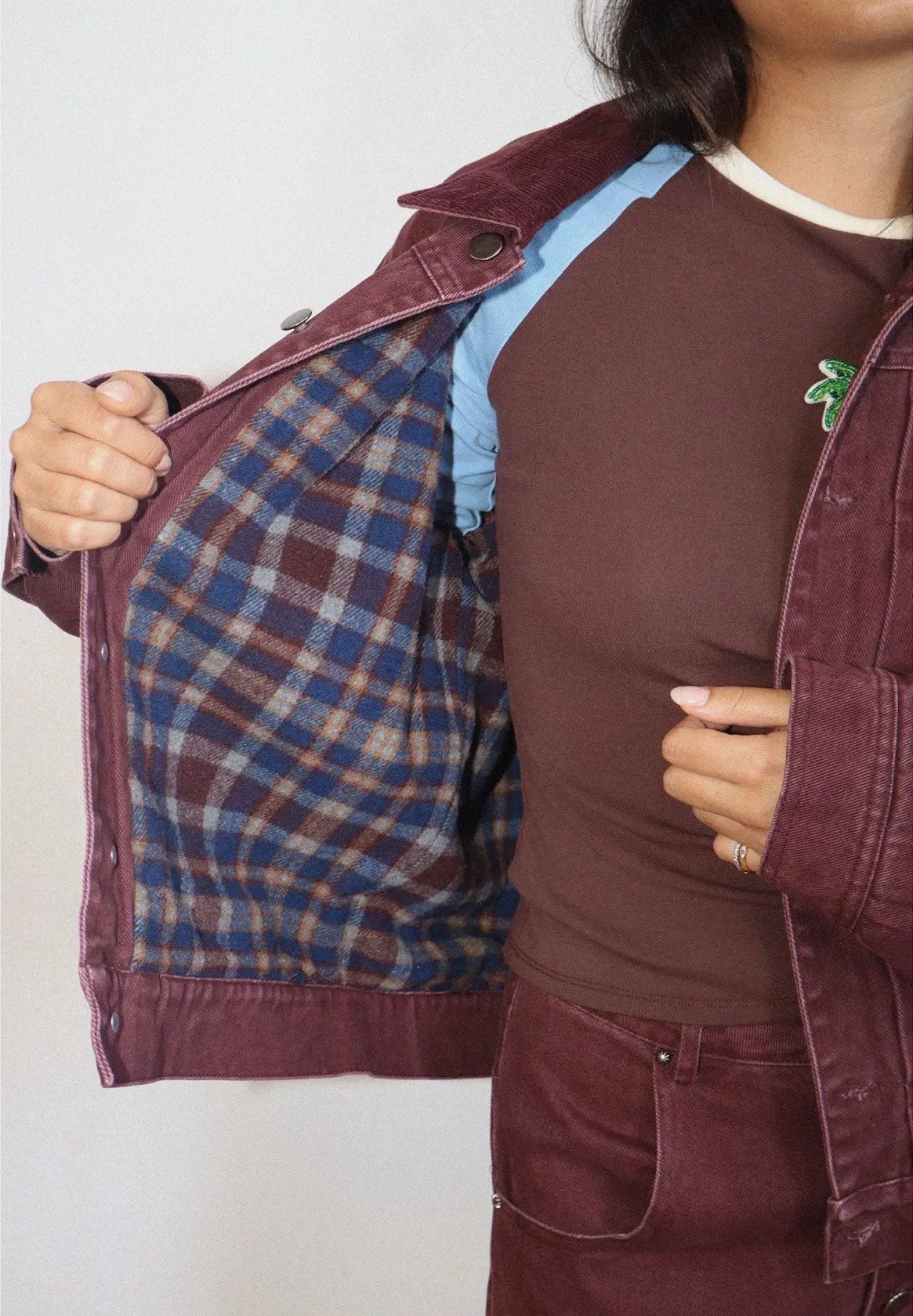 Burgundy flannel-lined denim bomber jacket shown open, revealing blue plaid interior lining, styled with matching trousers.