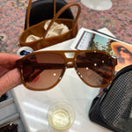 Hand holding oversized caramel brown aviator sunglasses with warm brown gradient lenses and gold hardware