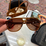 Hand holding oversized caramel brown aviator sunglasses with warm brown gradient lenses and gold hardware