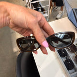 Hand holding DIFF Raya chocolate tortoise cat-eye sunglasses with dark tinted lenses at boutique display