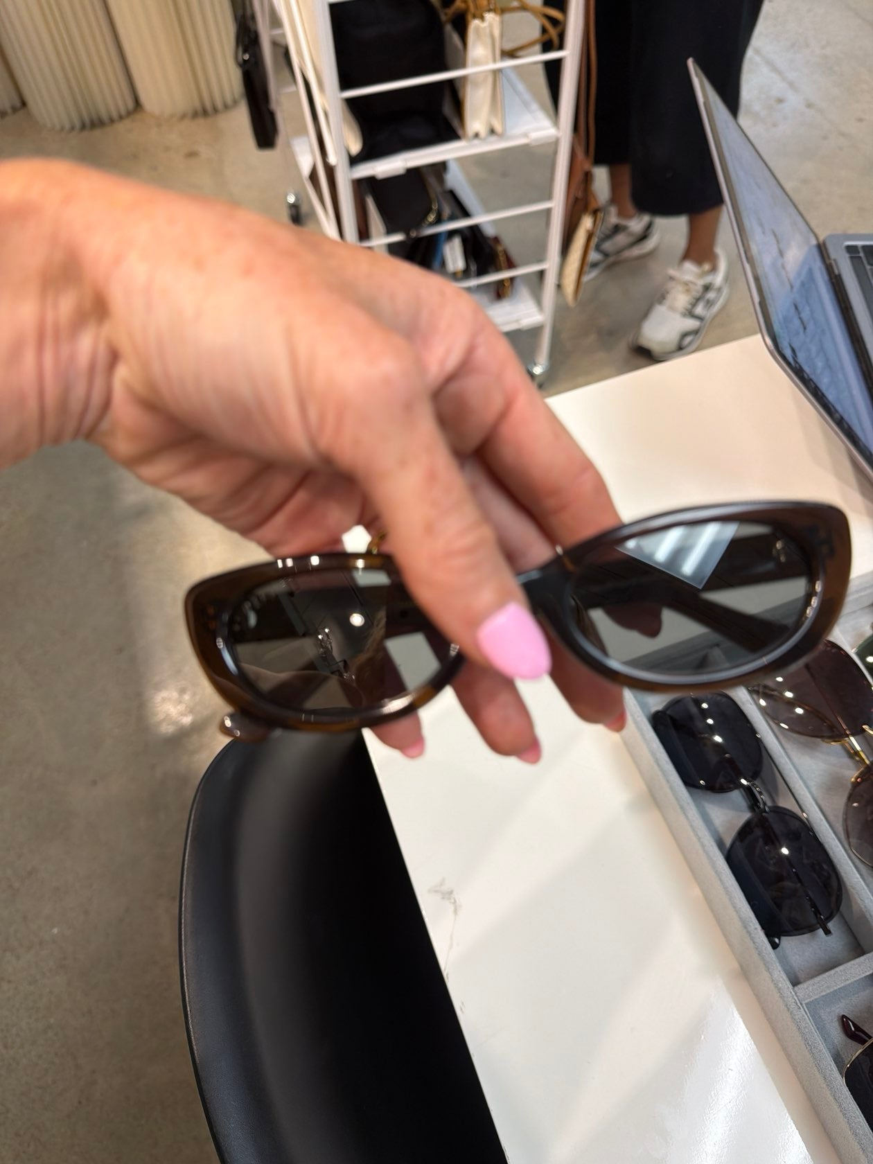 Hand holding DIFF Raya chocolate tortoise cat-eye sunglasses with dark tinted lenses at boutique display