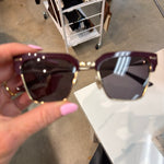 Deep cherry burgundy and gold half-rim square sunglasses held by hand with pink nails