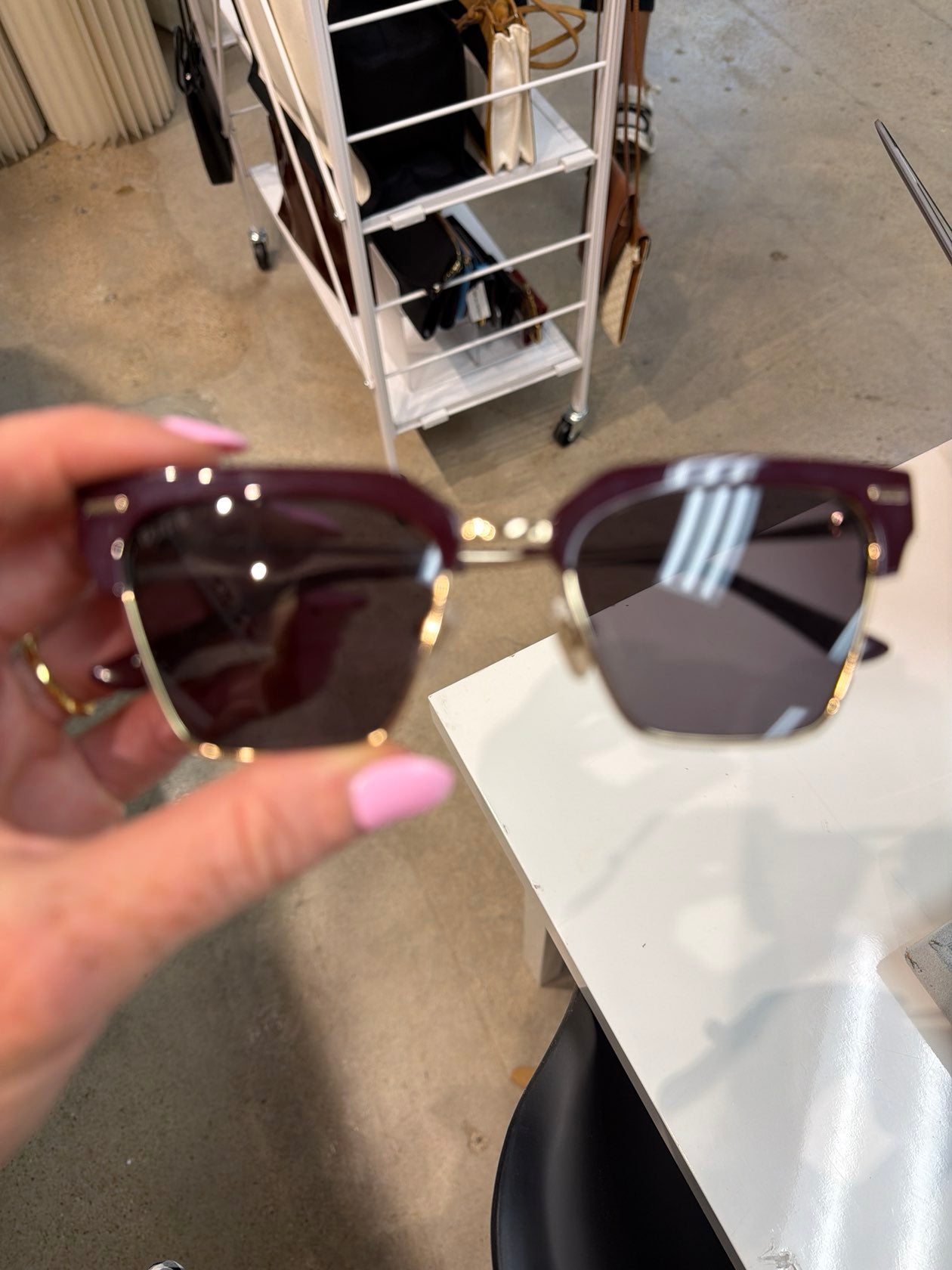 Deep cherry burgundy and gold half-rim square sunglasses held by hand with pink nails