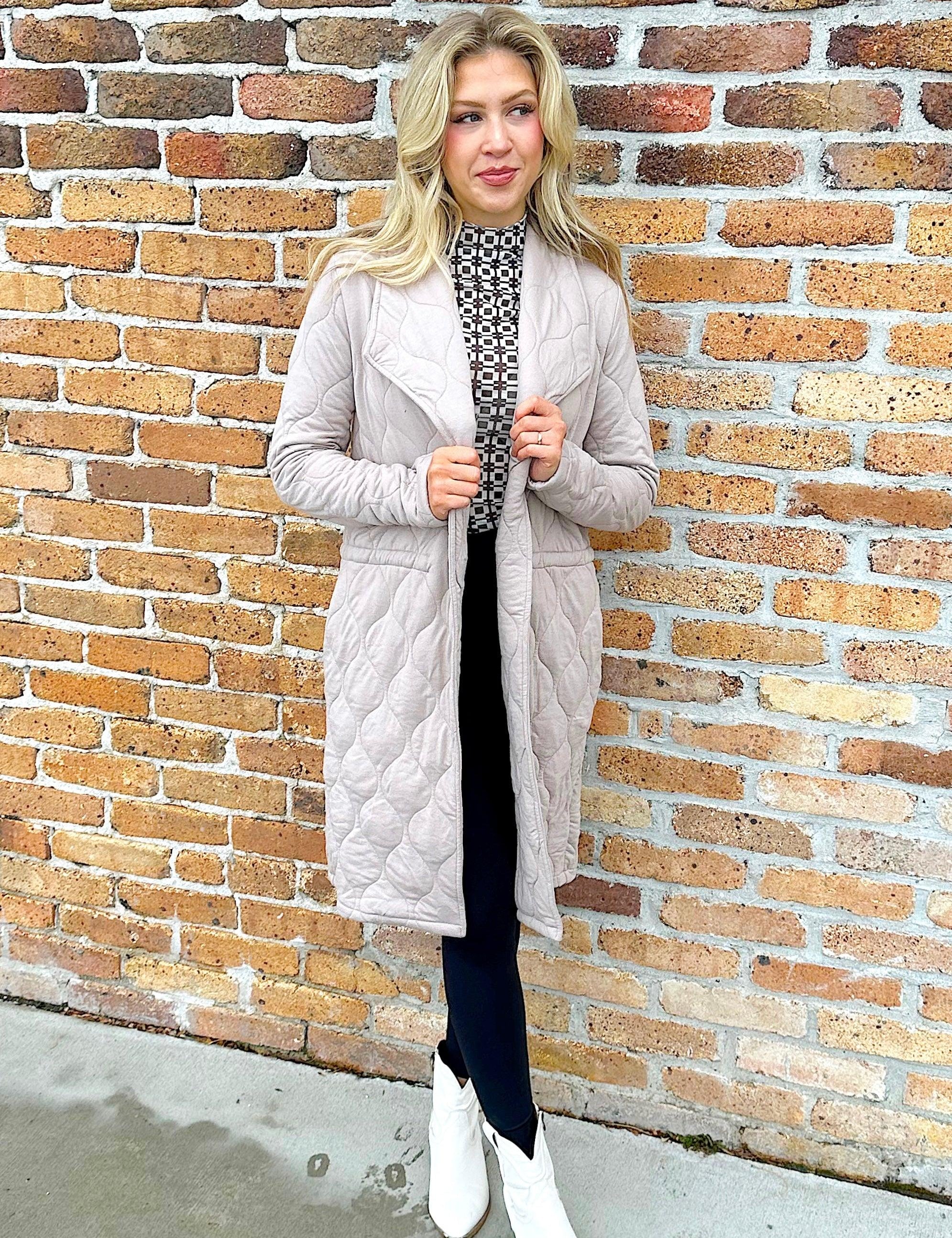 woman wearing quilted taupe long jacket. brand Steve Madden with a drawstring to cinch at waist for more fitted apperance 